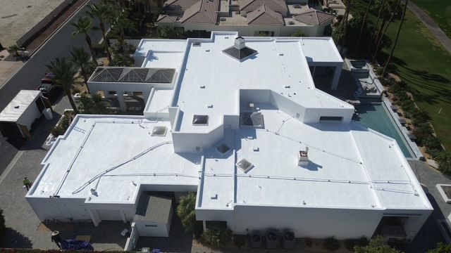 Aerial view of a modern, white-roofed home with a pool. The house has a flat roof and multiple levels.
