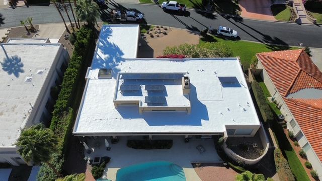 Aerial view of a white roof on a home with a swimming pool, set in a residential area with palm trees and cars.
