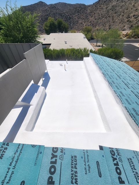 A flat white roof under construction with blue underlayment visible on the edges, and a mountain backdrop.