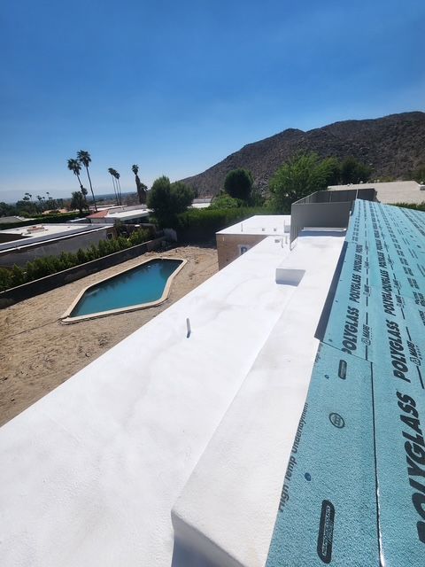 View of a white roof under construction, overlooking a pool and desert landscape with mountains in the background. Blue sky.
