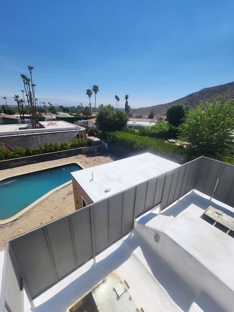 View from a rooftop overlooking a turquoise pool, green landscaping, and distant mountains under a bright blue sky.