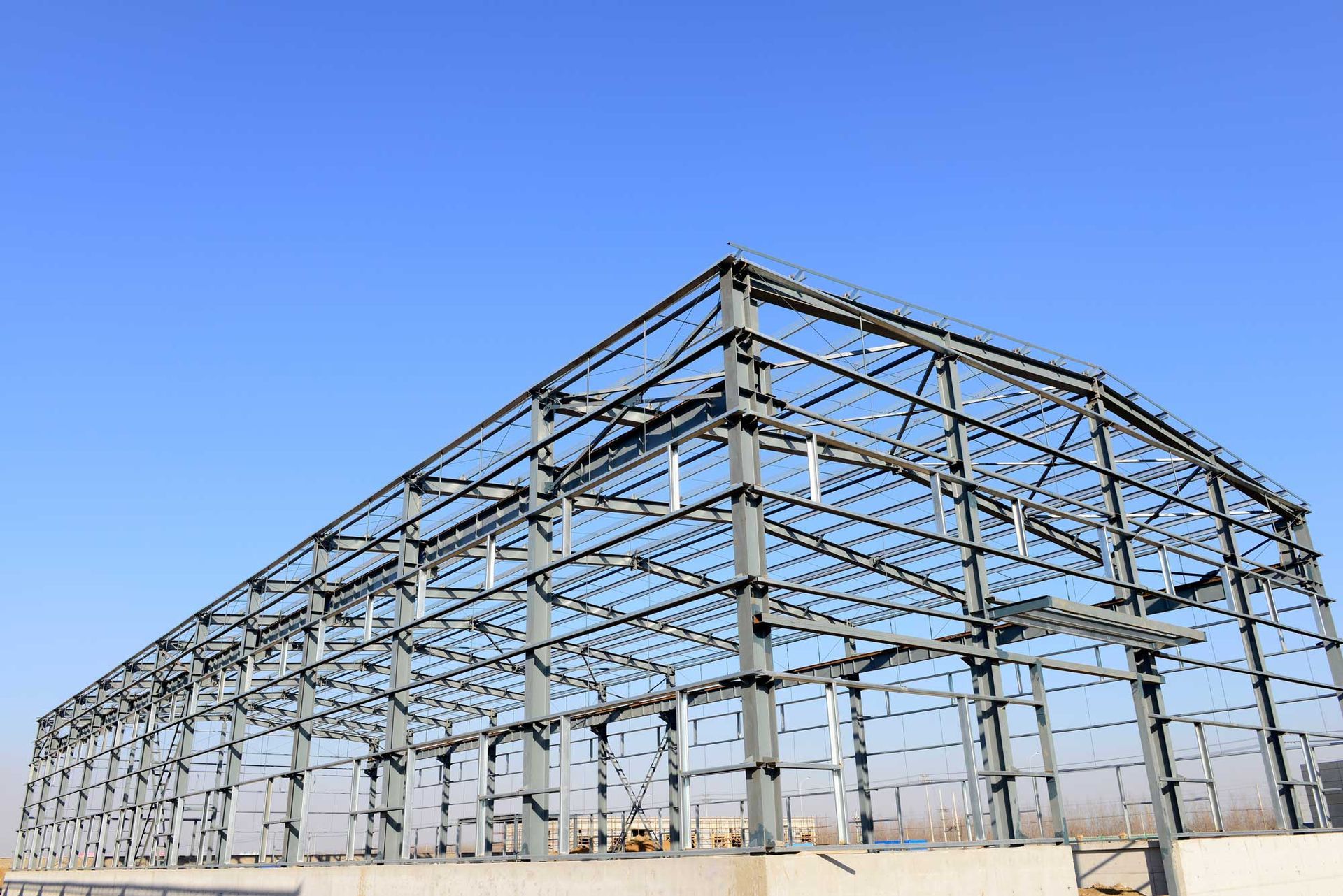 Steel framework of a large industrial building under construction against a clear blue sky.