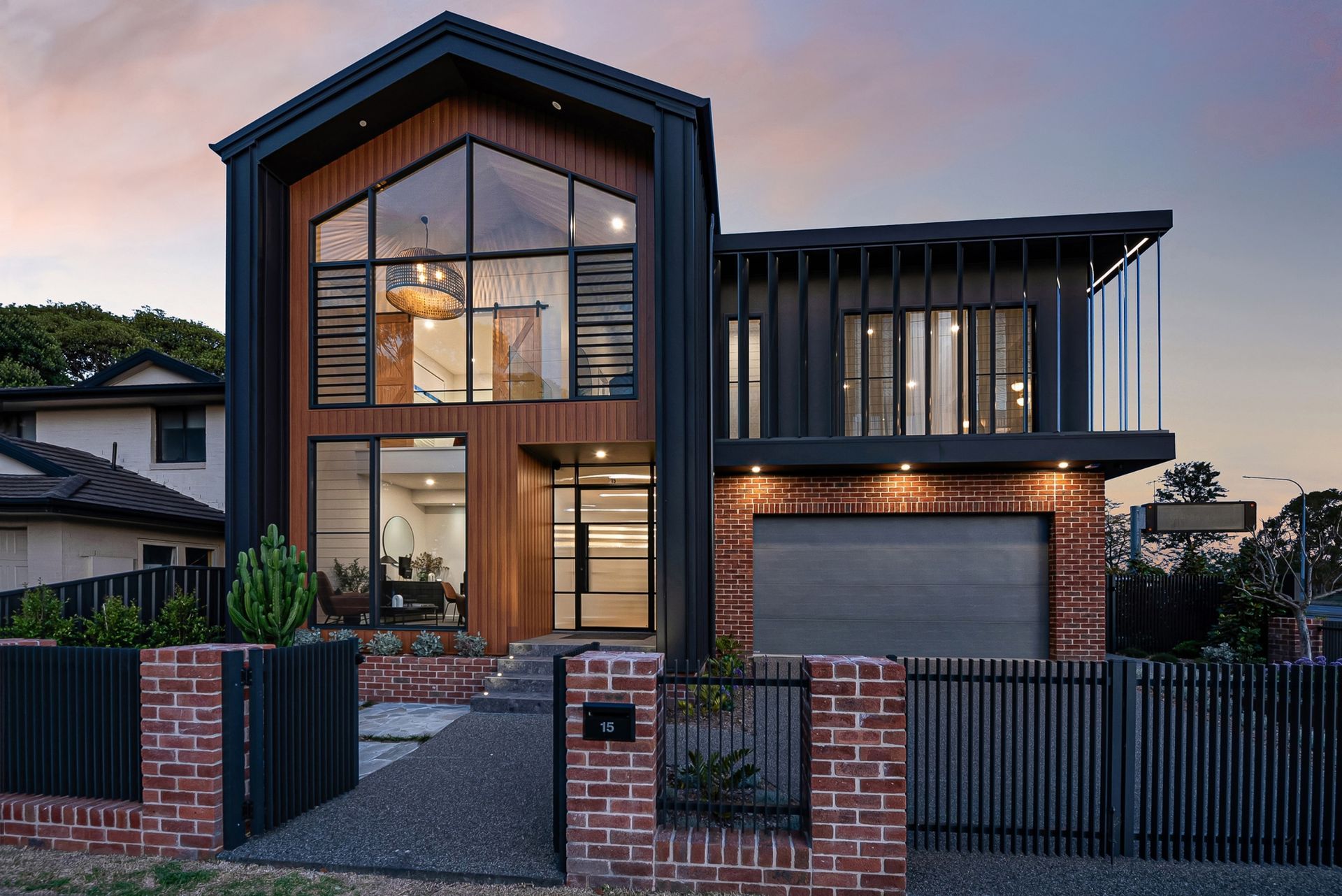 Modern two-storey custom home facade with timber cladding, brickwork, large windows and a black front fence.