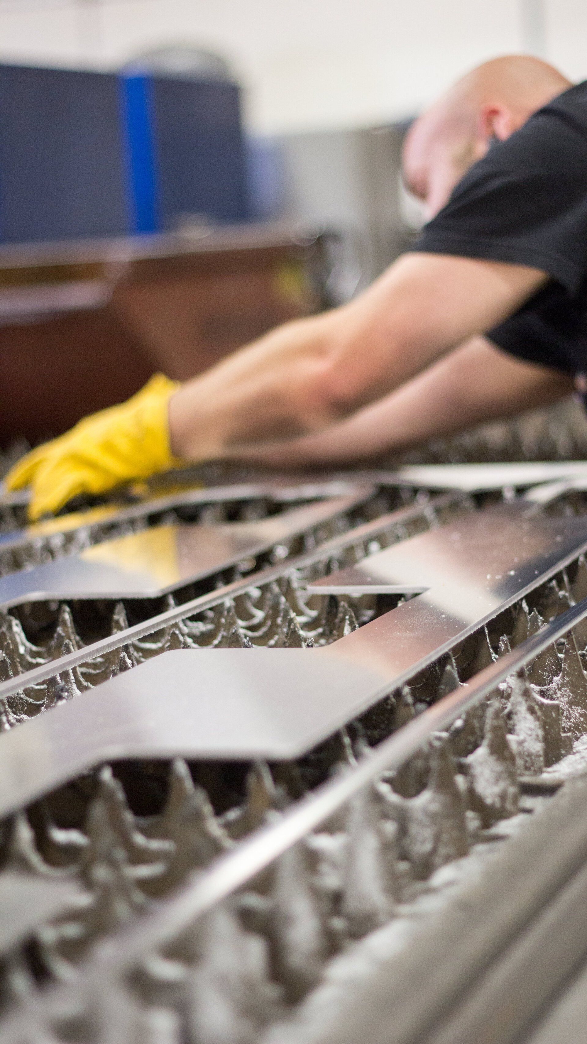 A man wearing yellow gloves is working on a machine in a factory.