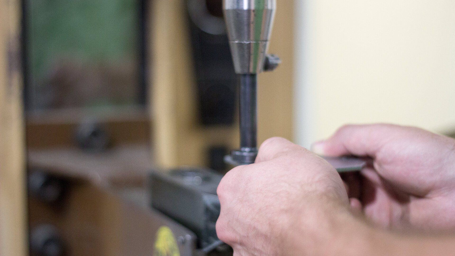A close-up of a person holding a piece of metal, feeding it into a fabricating machine.