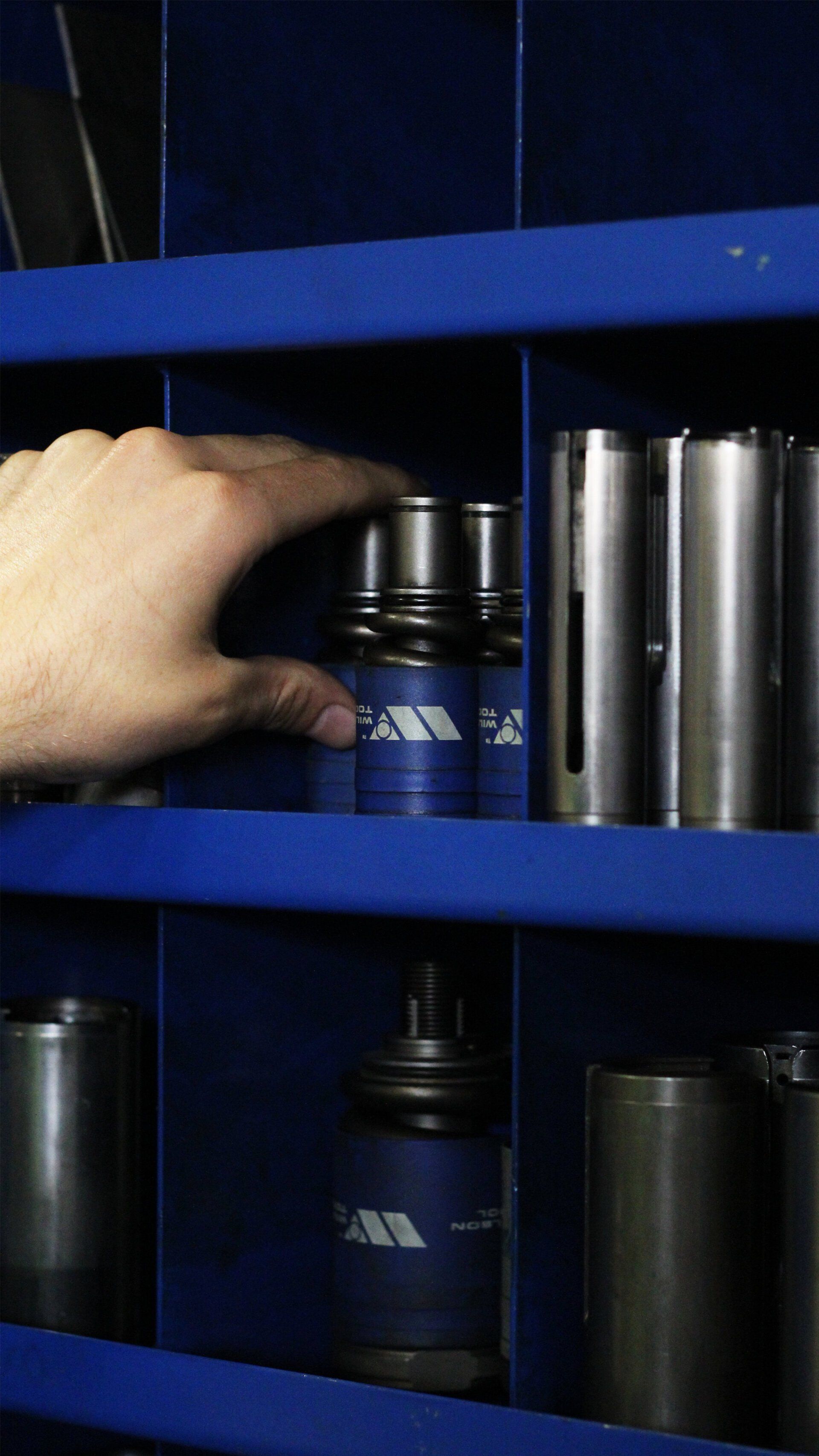 A person's hand is reaching into a blue shelf filled with metal tools.