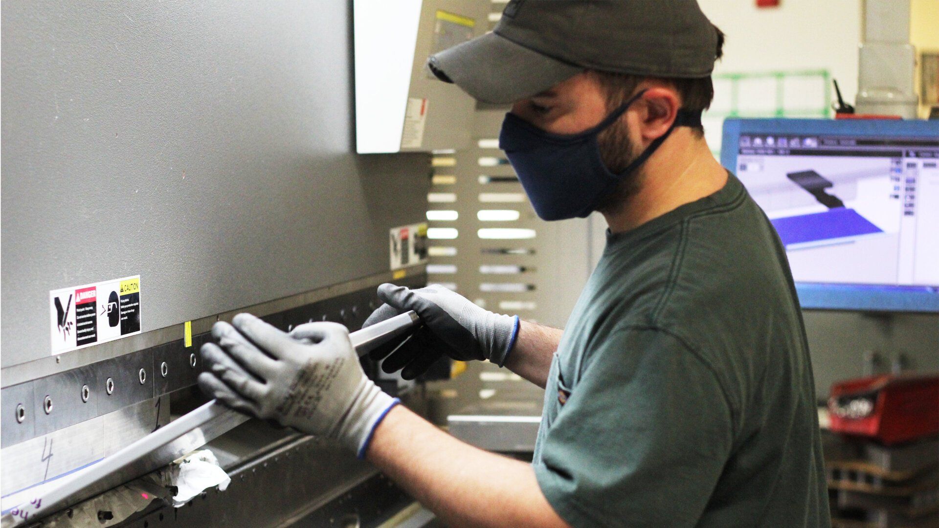A man wearing a mask and gloves is working on a metal fabricating machine.