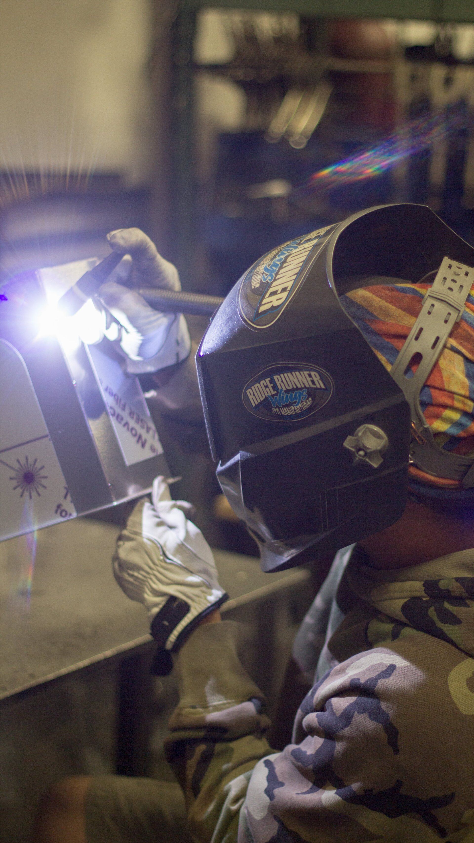 A man wearing a welding helmet is welding a piece of metal.
