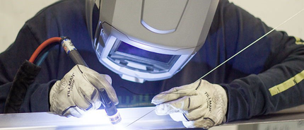A man wearing a welding helmet is welding a piece of metal.
