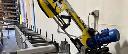 A yellow band saw is sitting in a warehouse next to a conveyor belt.