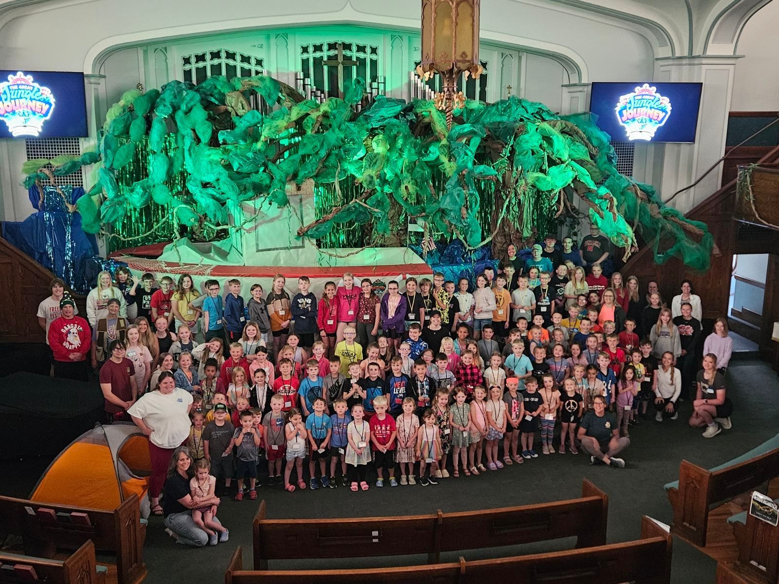 A group of kids are sitting at tables in a large room eating food at Worship on Wednesday