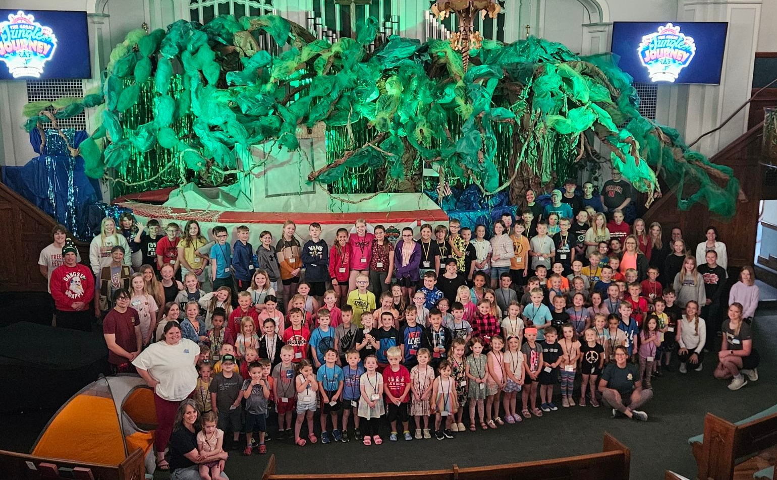 A group of kids are sitting at tables in a large room eating food at Worship on Wednesday