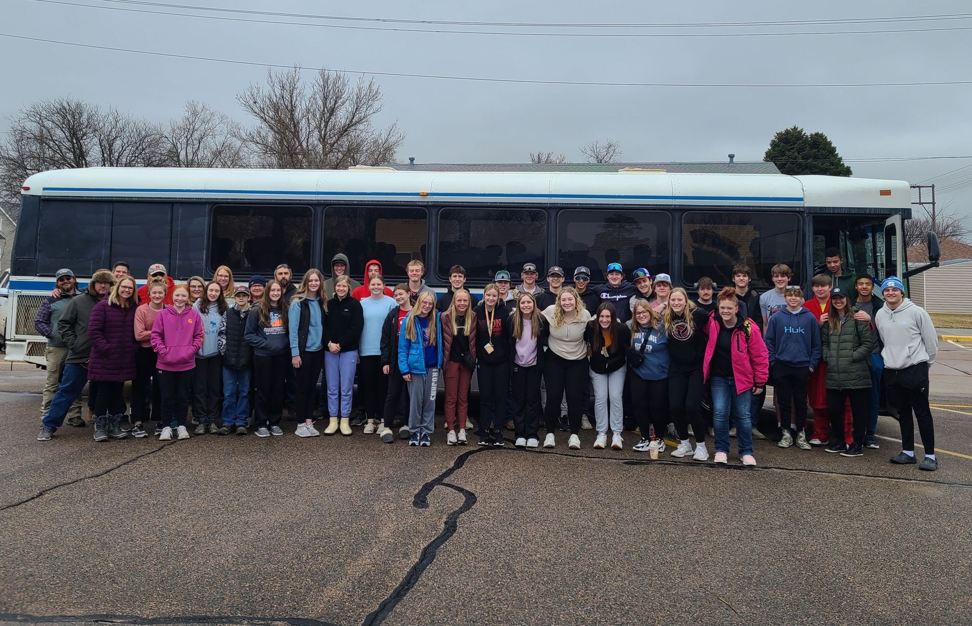 A group of people are posing for a picture in front of a bus heading to ski trip in Wyoming.