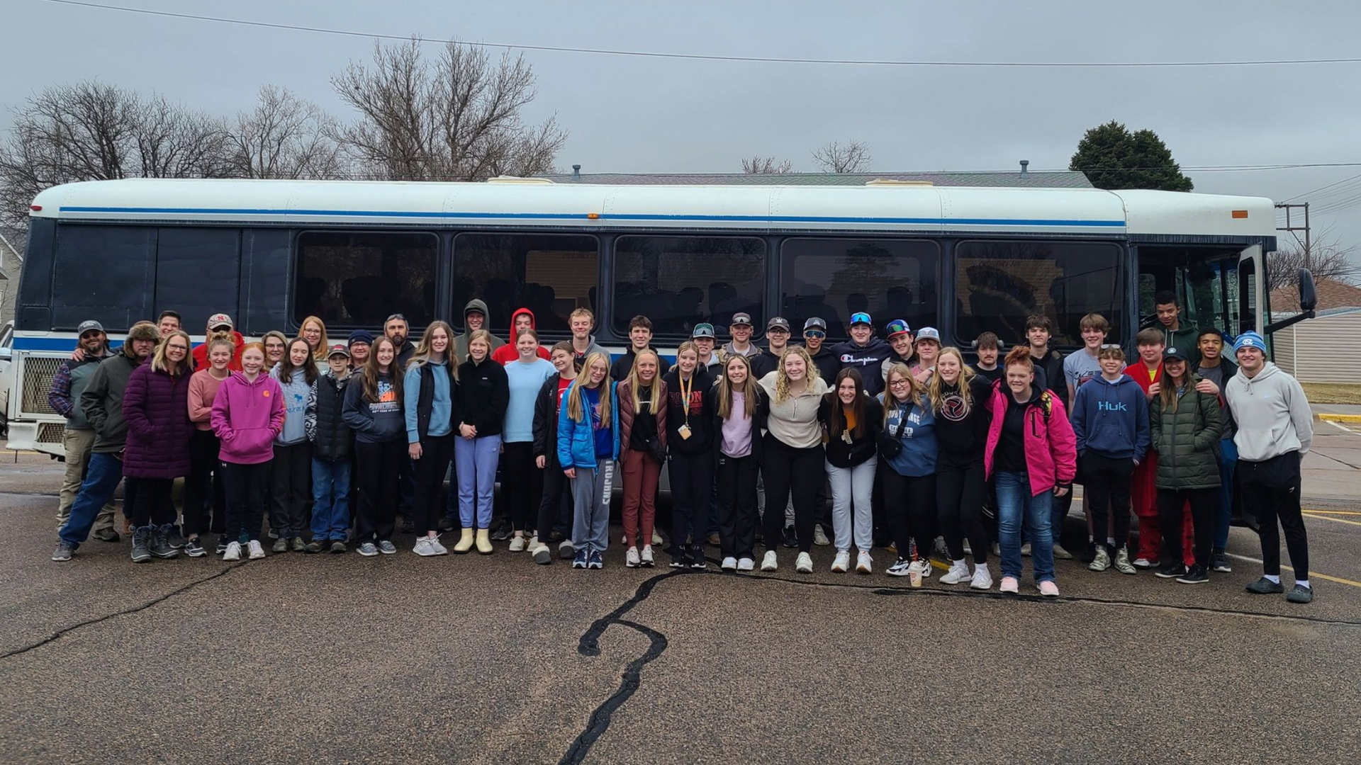 A group of people are posing for a picture in front of a bus heading to ski trip in Wyoming.