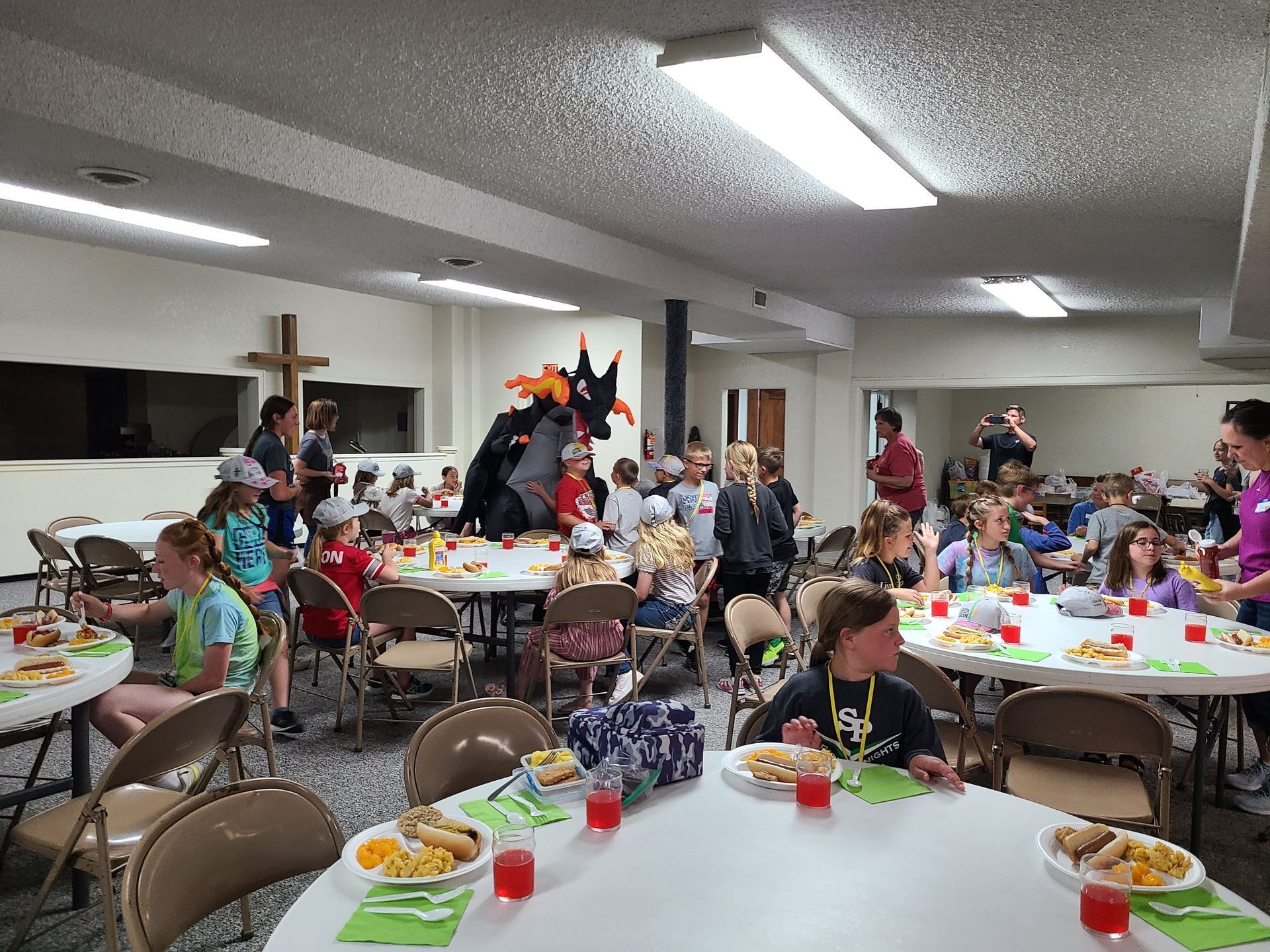 A group of kids are sitting at tables in a large room eating food at Worship on Wednesday