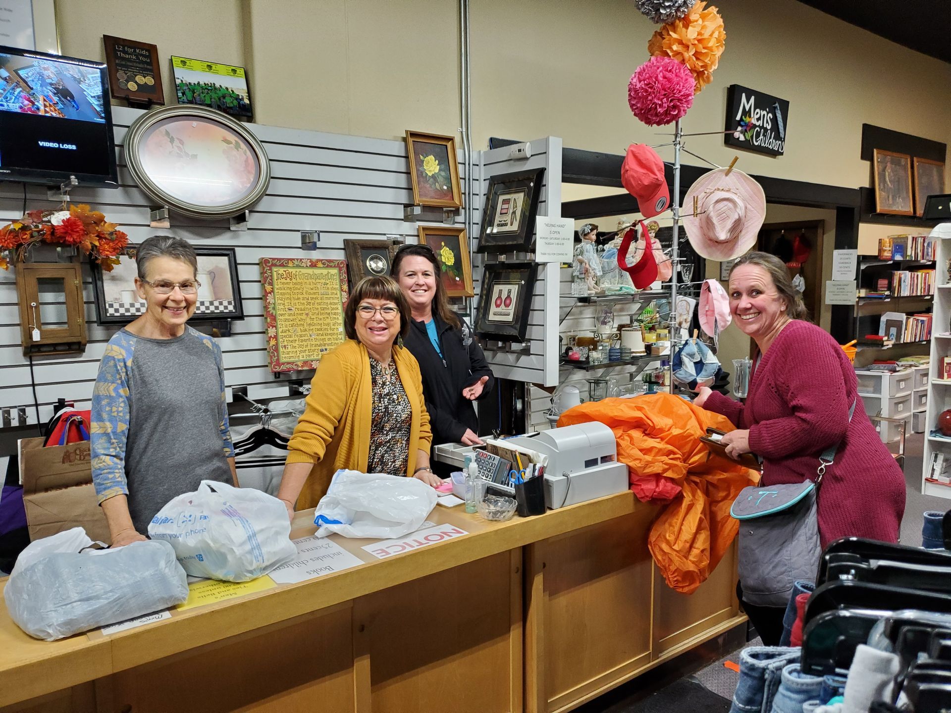 A group of women are standing behind a counter at Helping Hand Thrift Store.