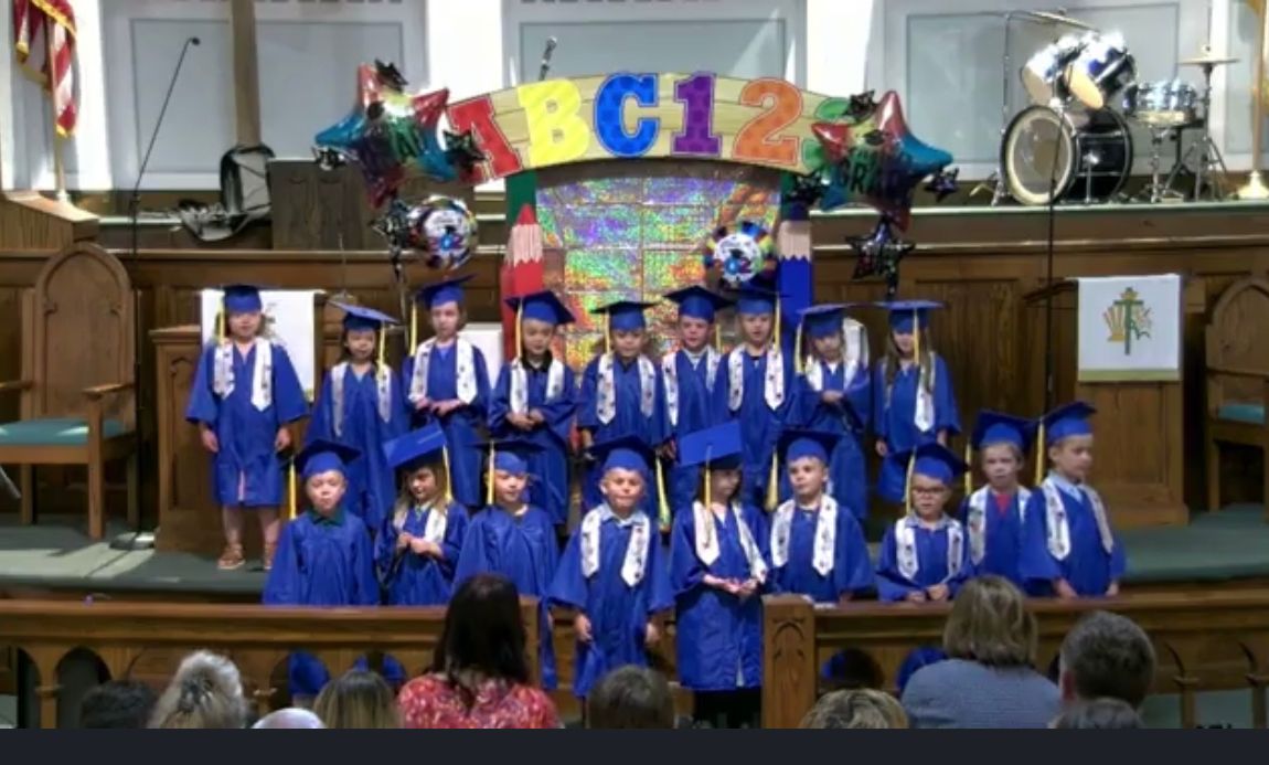 A group of children in graduation caps and gowns are standing in front of a sign that says abc123