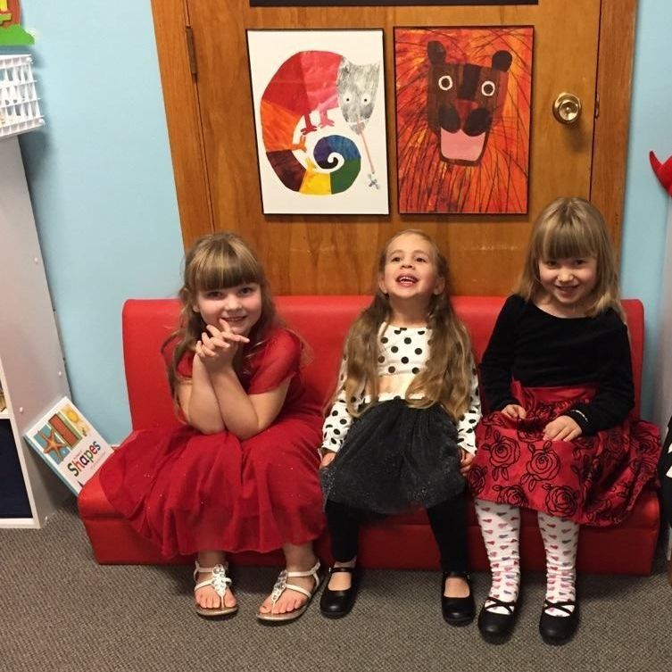 Three little girls are sitting on a red couch in a room