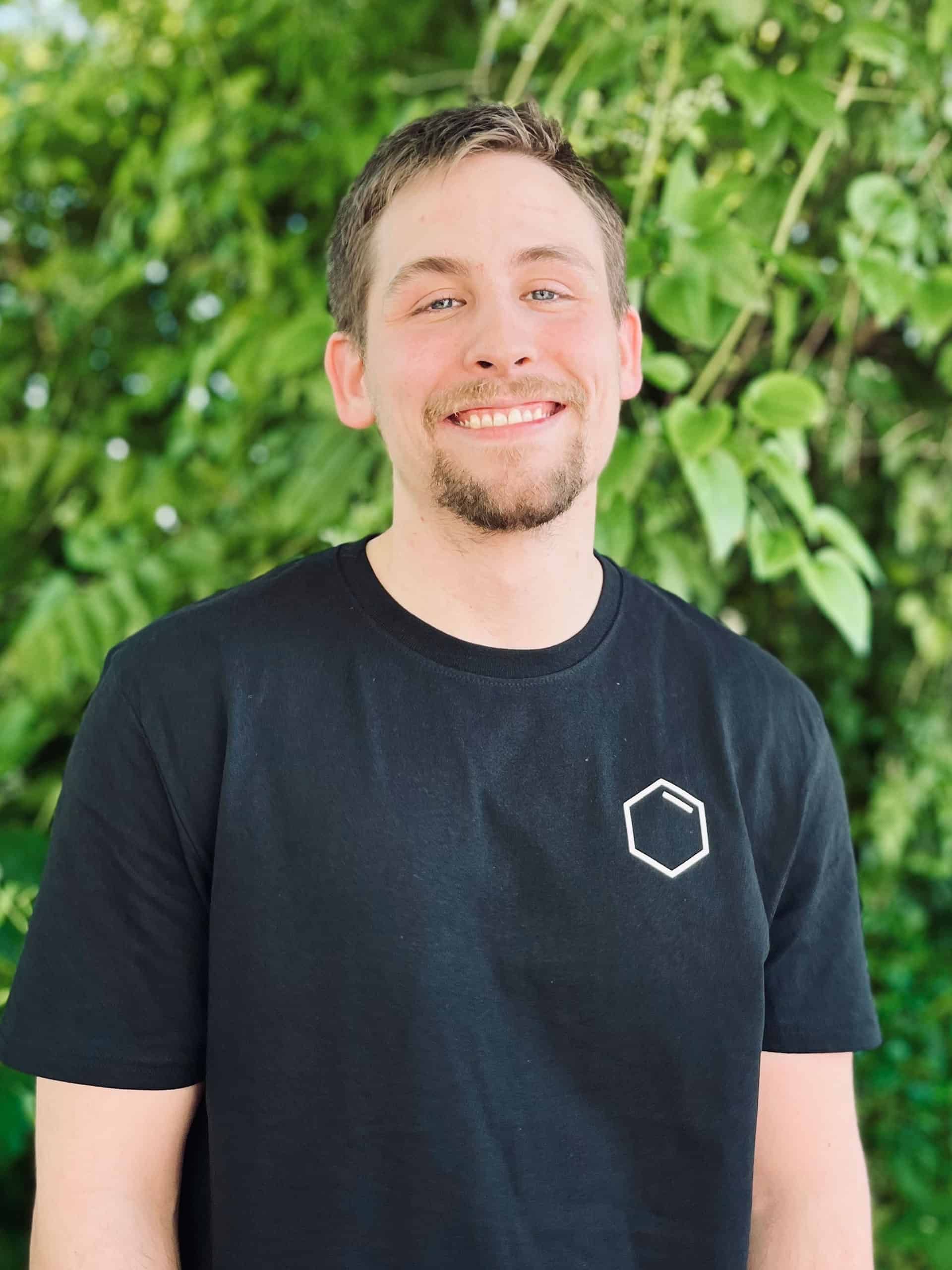 A man with a beard is wearing a black t-shirt and smiling.