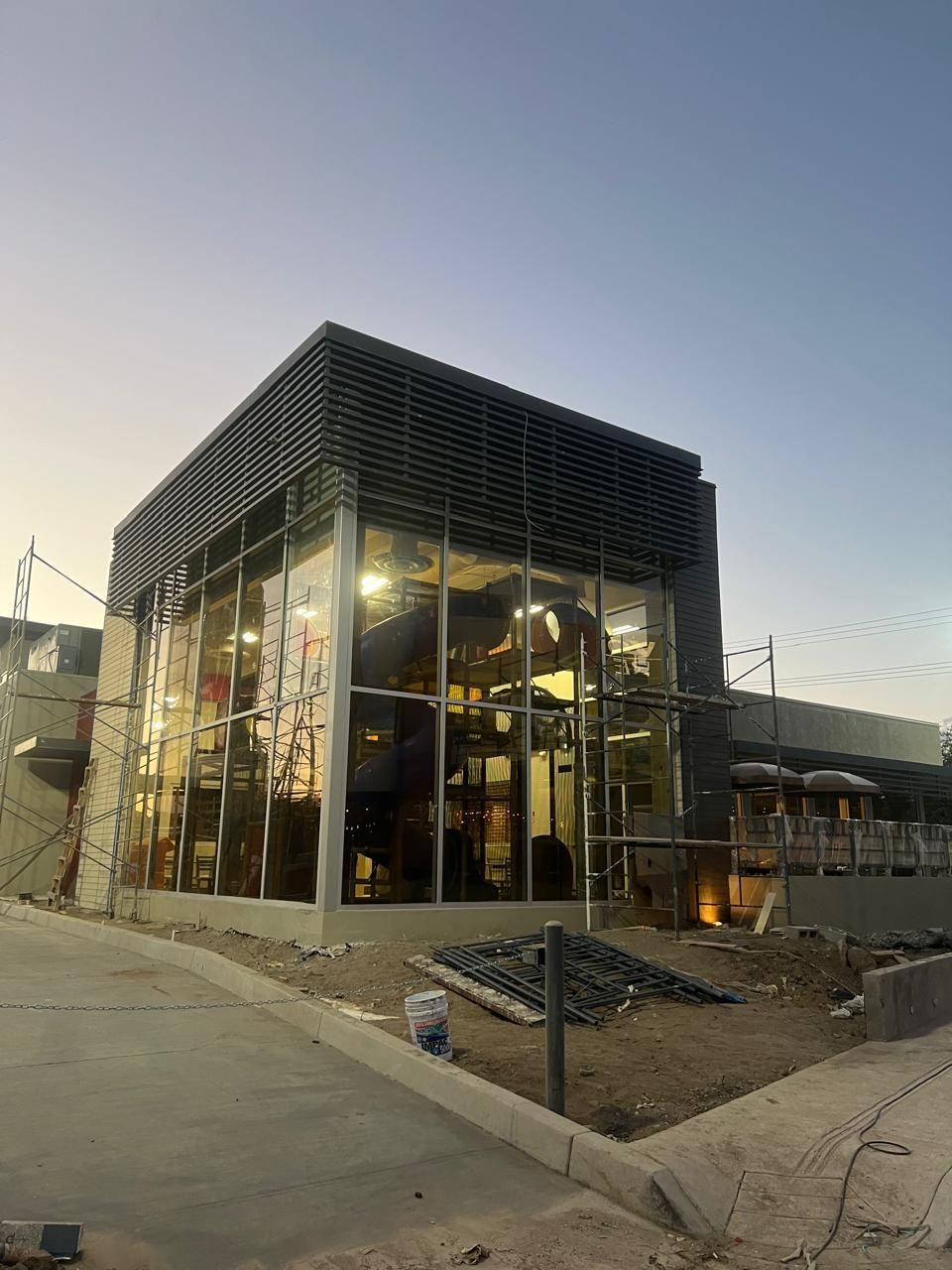 Obra en construcción, edificio moderno con paredes de cristal, iluminación al anochecer.