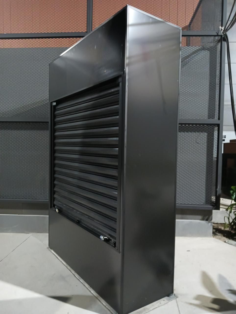 Mueble metálico de color negro con lamas horizontales, para exterior.