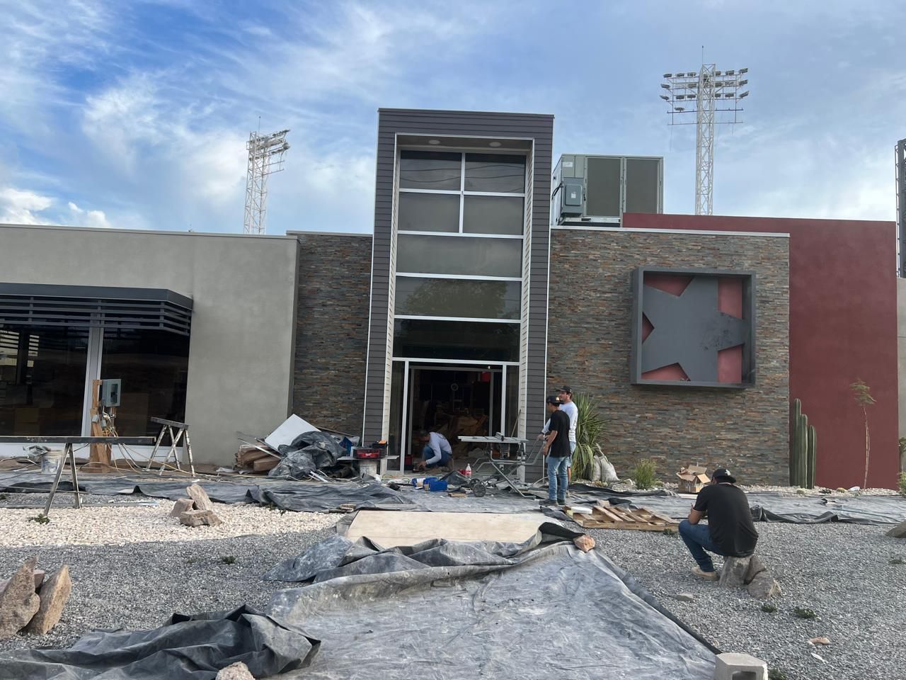 Exterior de un edificio con ventanas rotas, escombros y gente inspeccionando los daños.