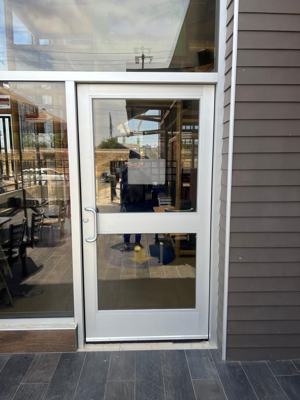 Puerta de cristal con marco plateado que refleja una escena exterior. Entrada a un edificio.