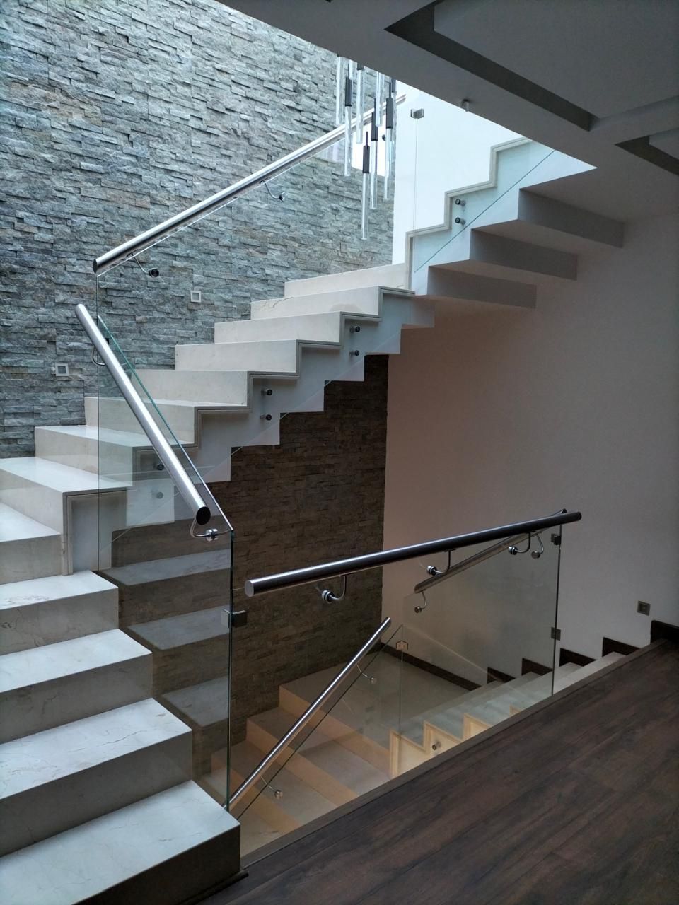 Escalera moderna con escalones de hormigón, barandilla de acero inoxidable y fondo de pared de piedra.