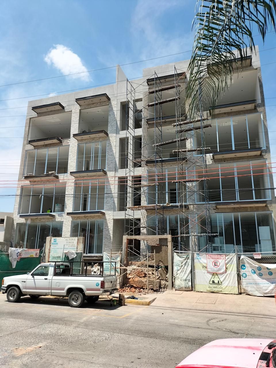 Edificio de varios pisos en construcción con un camión blanco estacionado en frente.