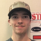 Man wearing a camouflage and American flag hat smiles in front of a sign with the word