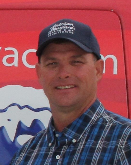 Man in cap and plaid shirt smiles in front of a red vehicle.