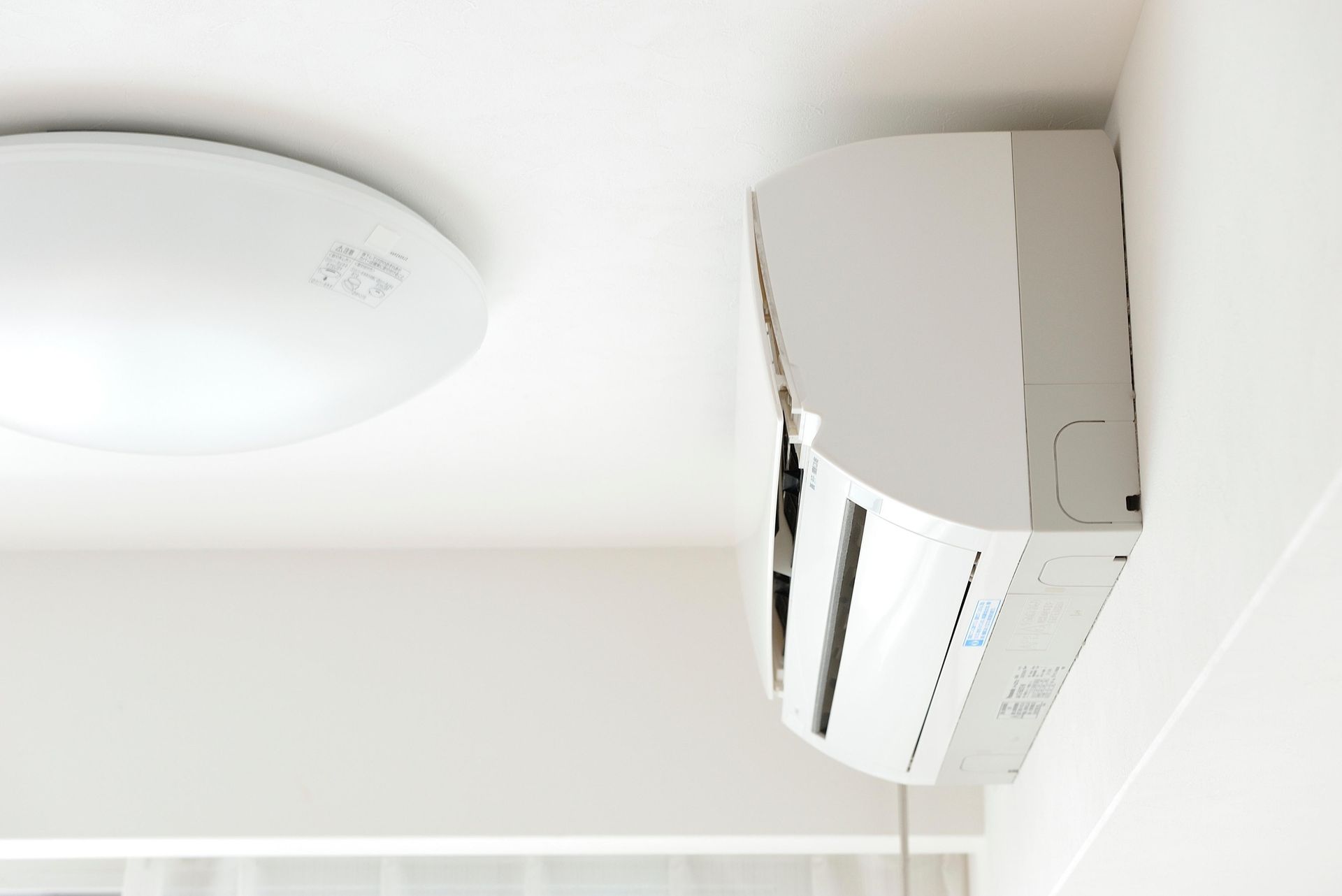 White wall-mounted air conditioner unit next to a white ceiling light.