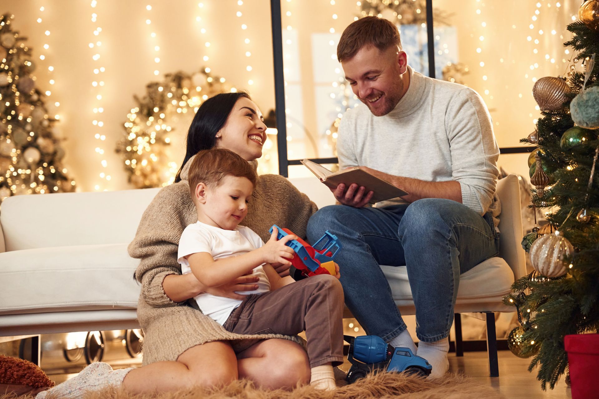 Family reading a book together near a Christmas tree. The mother and child are smiling while the father reads.