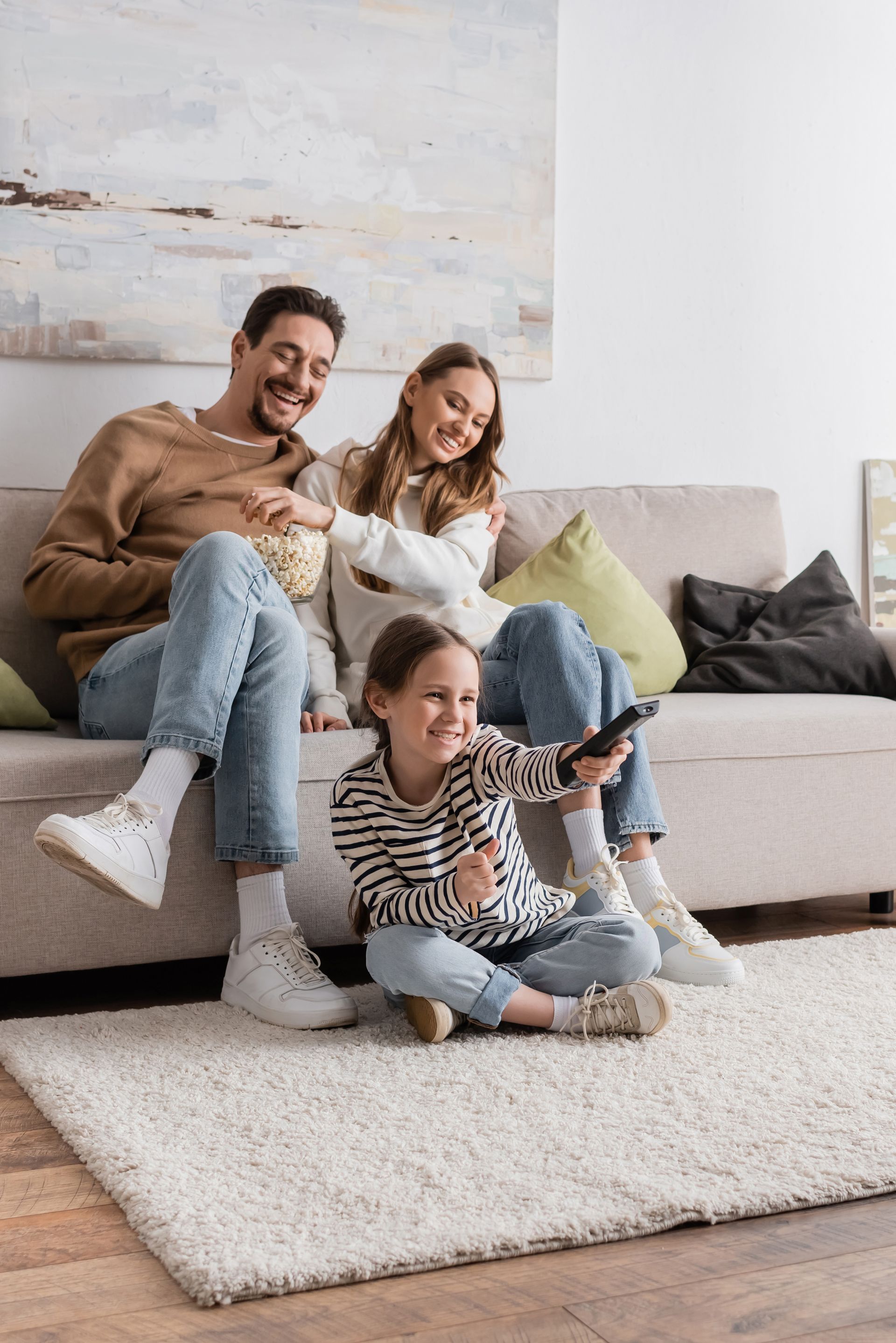 Family watches TV together on a couch, holding popcorn and a remote.