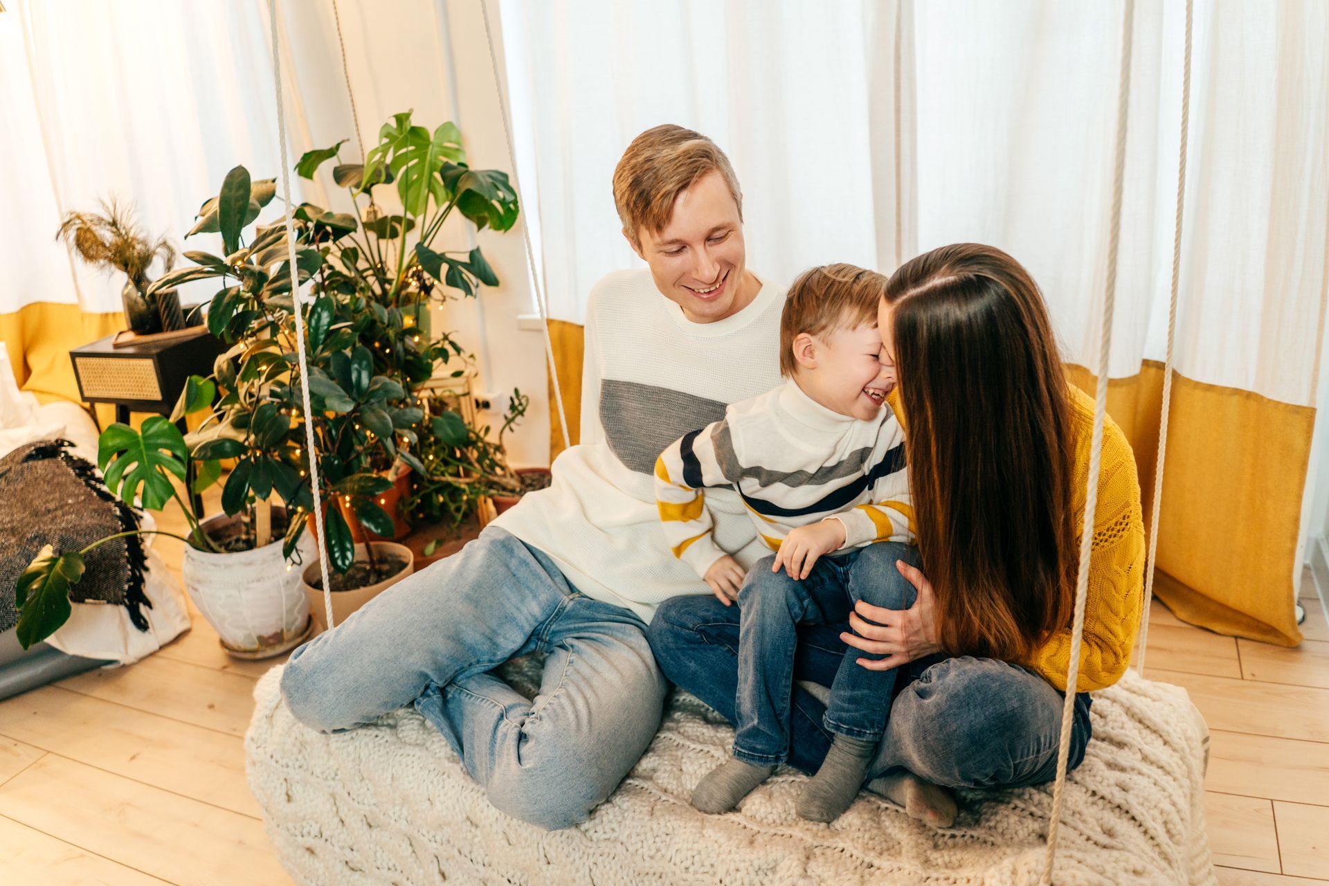 Family of three seated together on a swing; the child is between the parents, smiling.