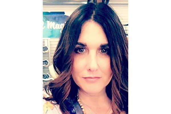 Woman with dark hair, brown highlights, looking at the camera. She's in a store with a blue and white sign behind her.
