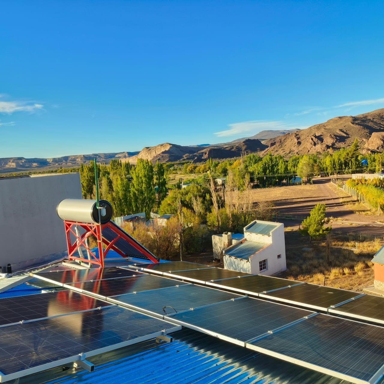 Paneles solares en la azotea y calentador de agua con un paisaje de montaña al fondo bajo un cielo azul.