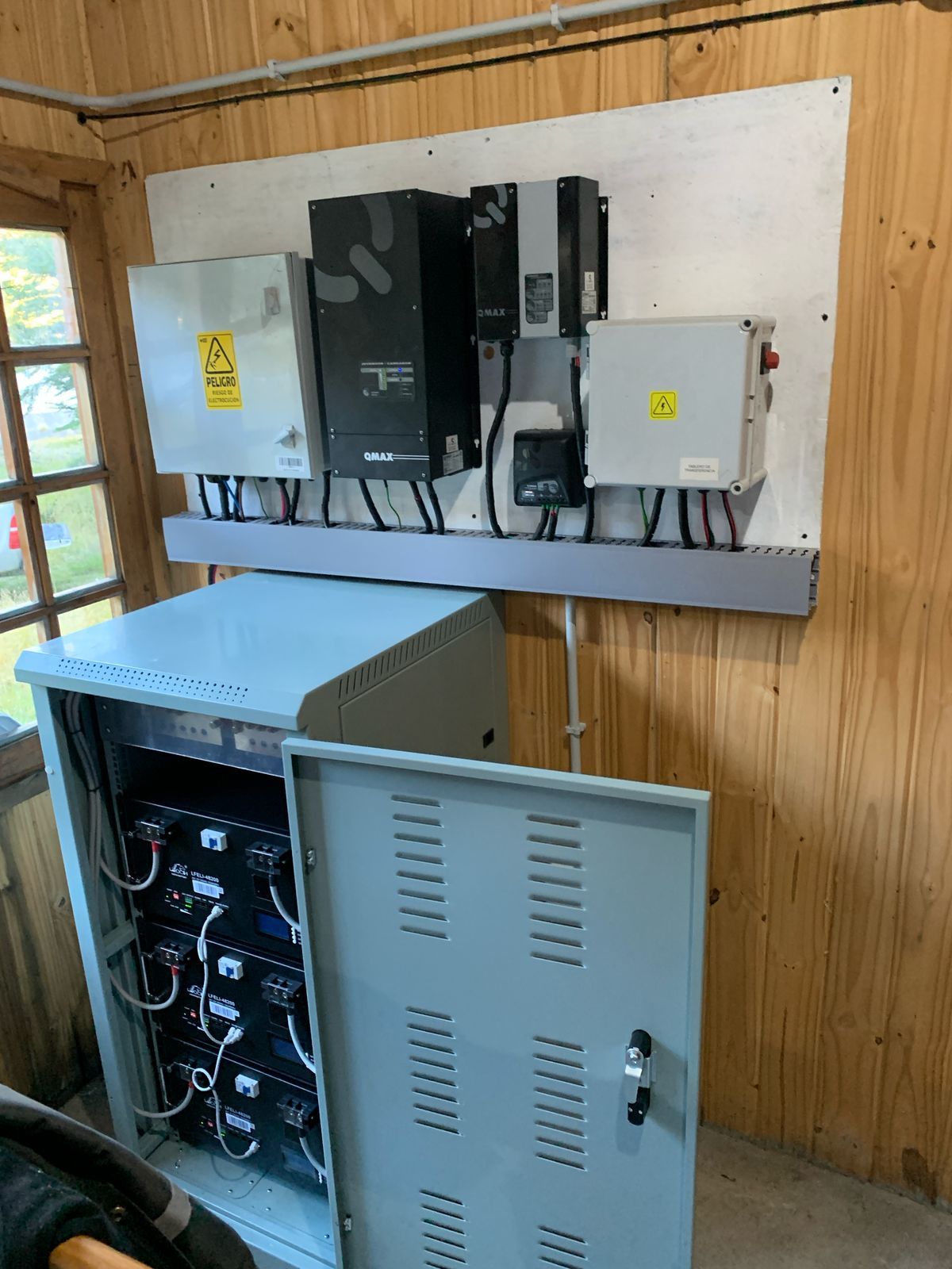 Componentes del sistema de energía solar montados sobre paneles de madera, incluidos inversores y baterías.