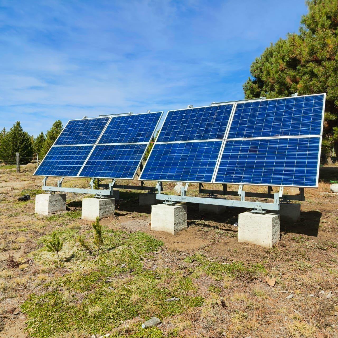 Paneles solares sobre bloques de hormigón en un campo, cielo azul al fondo.