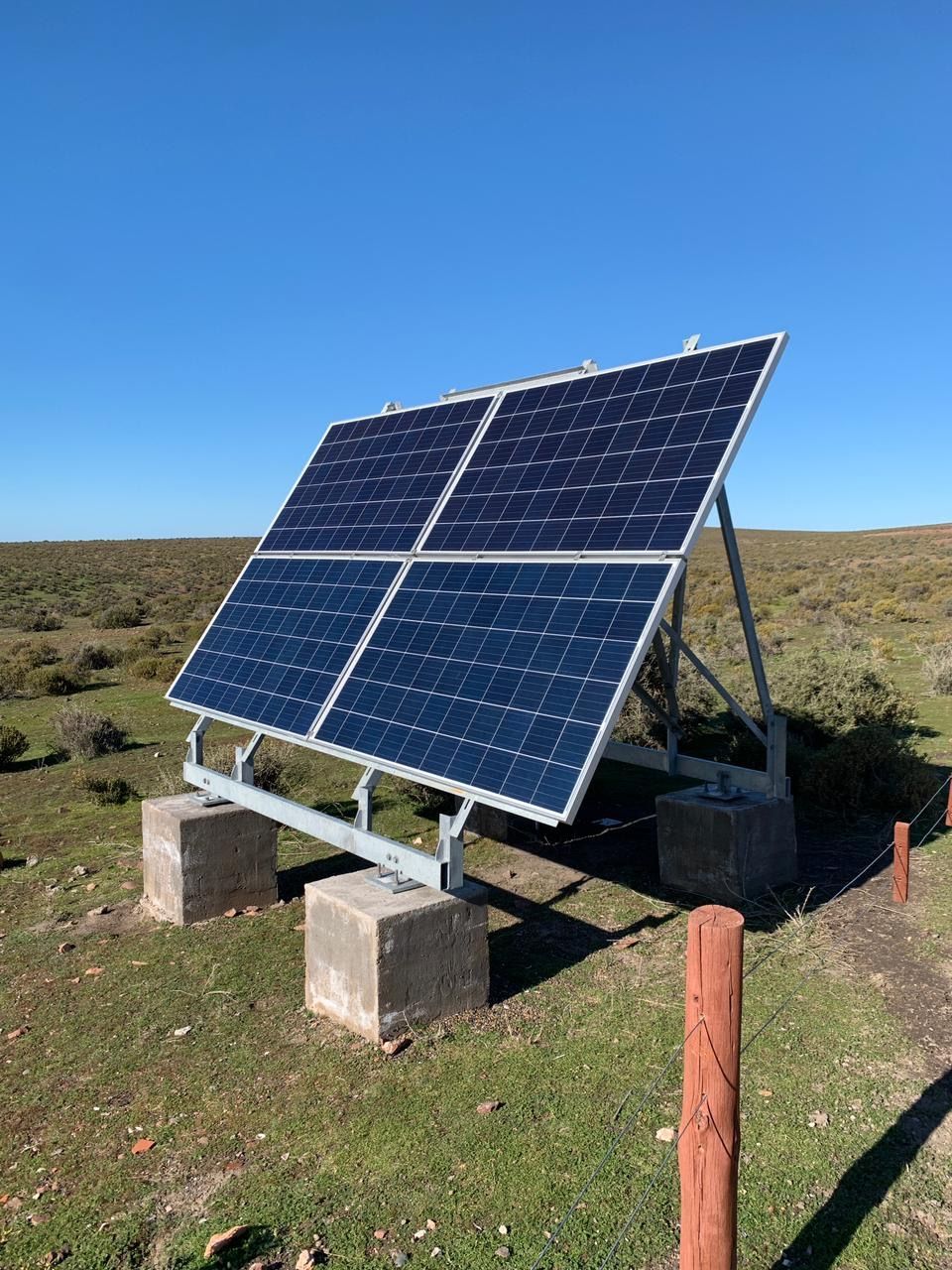 Conjunto de paneles solares sobre bloques de hormigón en un campo, orientados hacia un cielo azul.