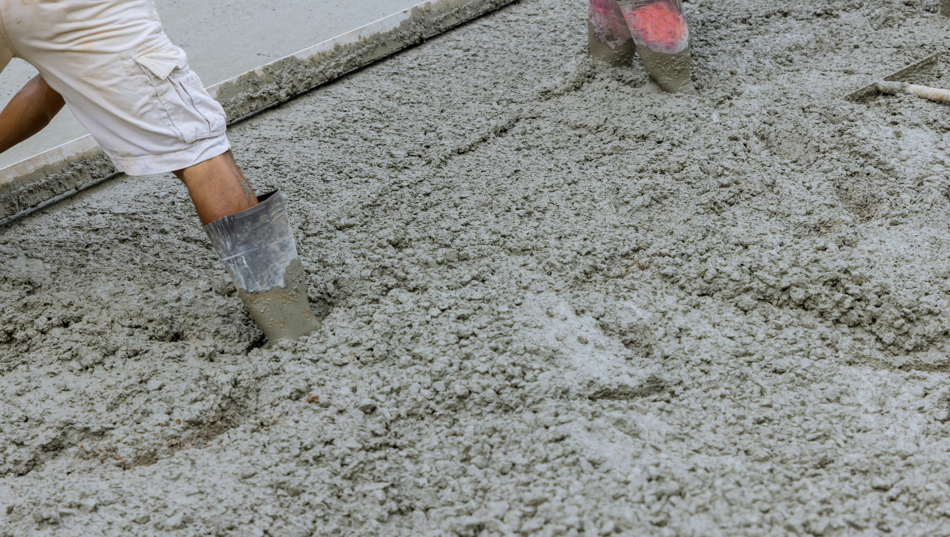 Person in boots smoothing wet concrete with a tool.