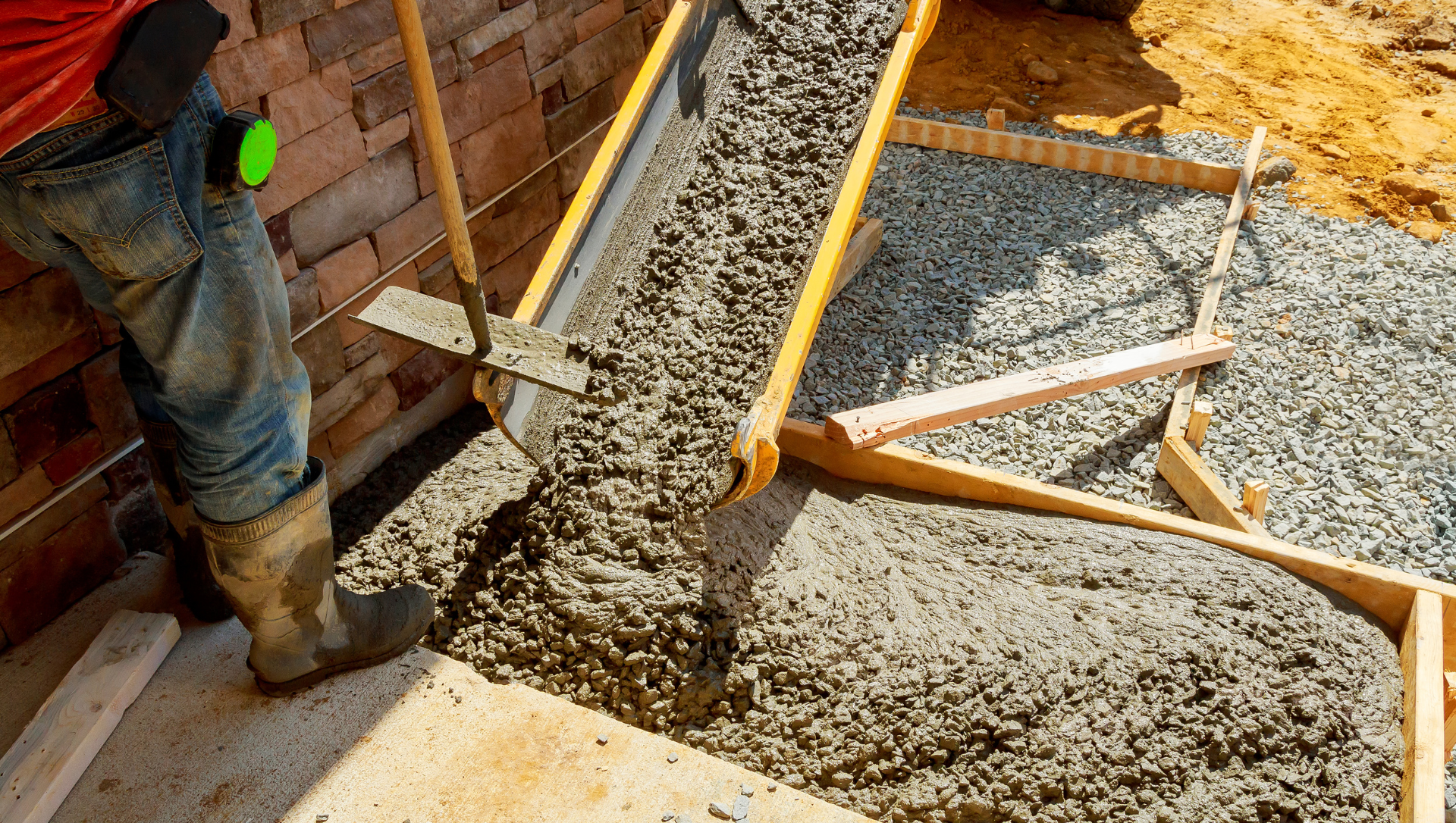Person pouring wet concrete from a chute into a wooden form, outside.