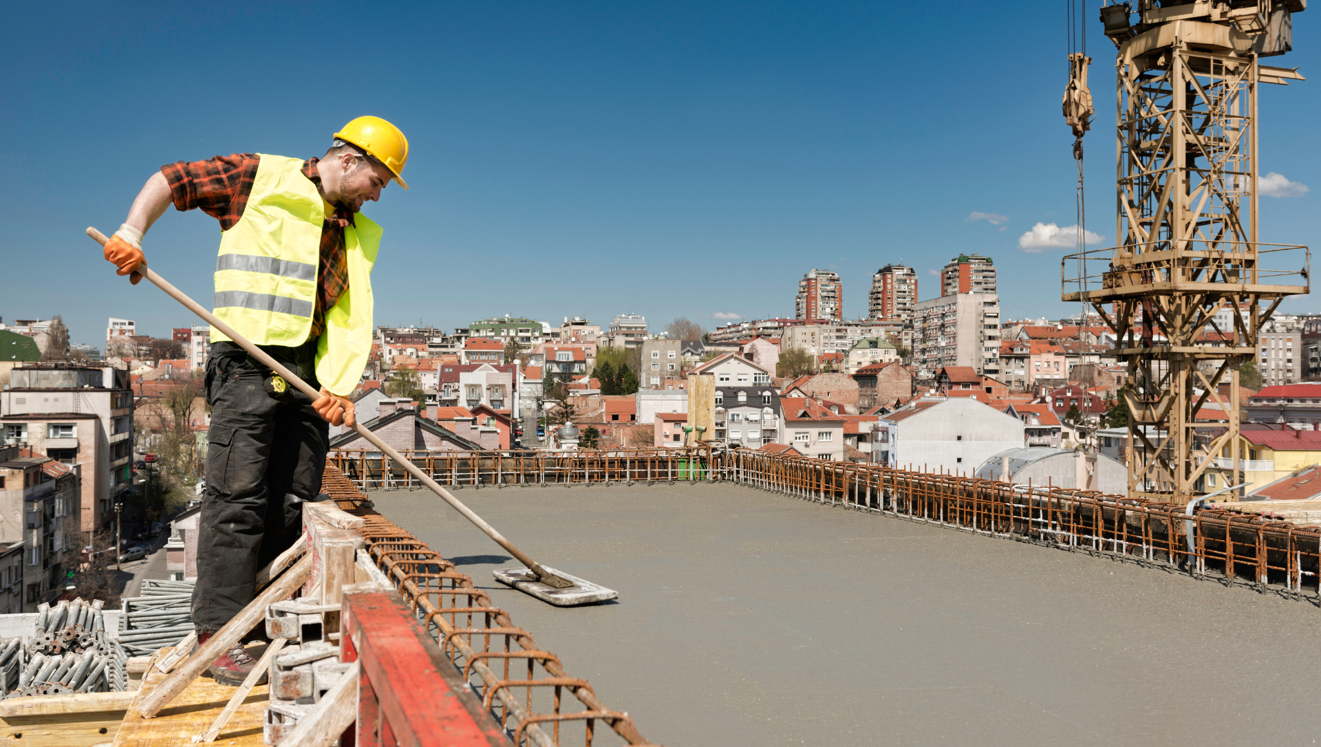 Construction worker spreading concrete on a rooftop with cityscape backdrop.
