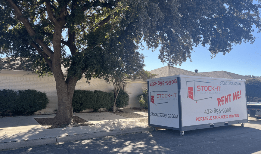 A storage container is parked in front of a house next to a tree.