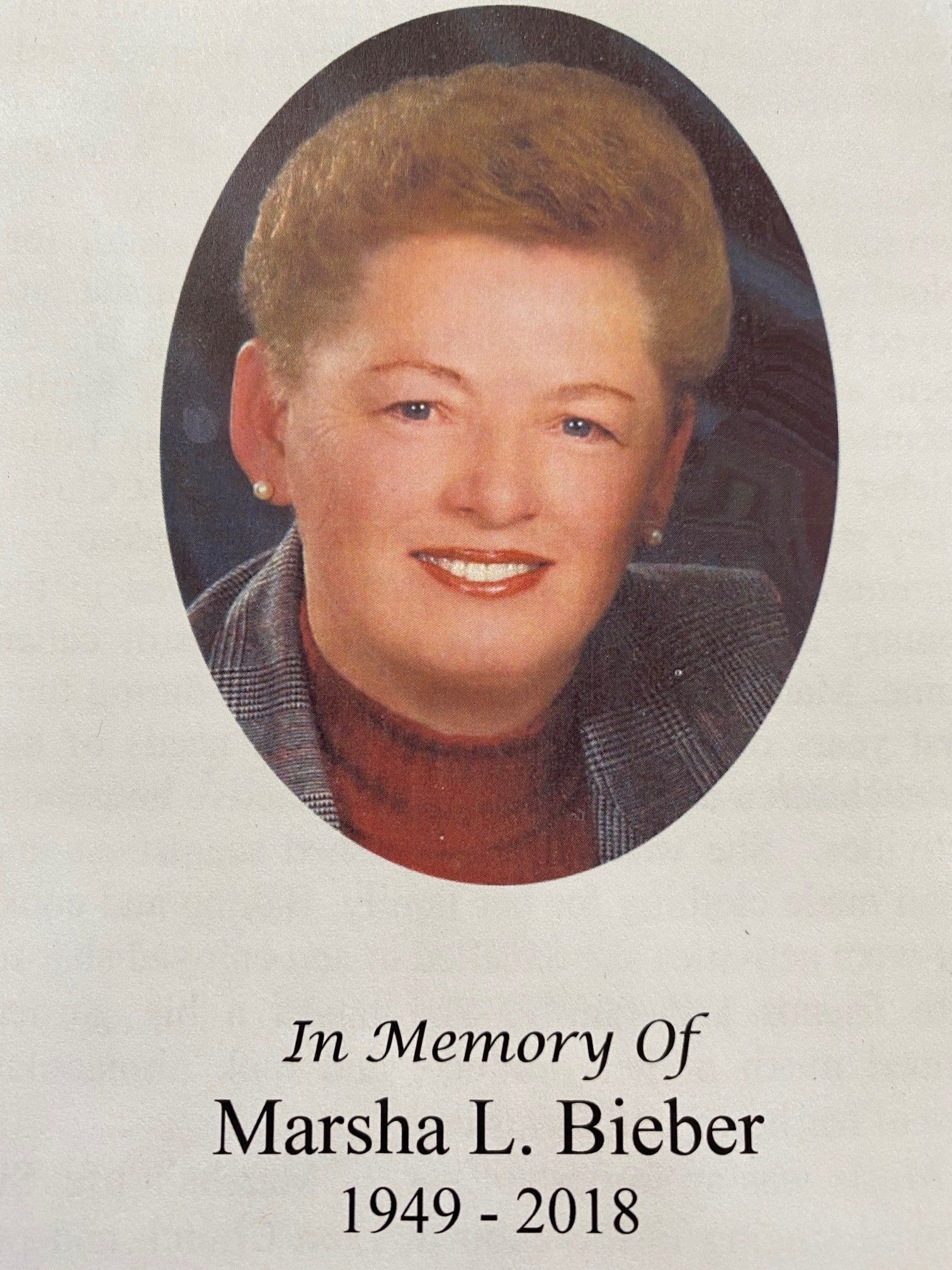 Oval portrait of Marsha L. Bieber (1949-2018), with short blonde hair and a red top.