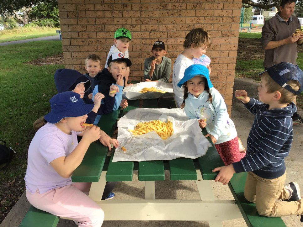 A Group of Children Are Sitting at a Picnic Table Eating French Fries — Earth Angels Child Care Centre in Tinonee, NSW
