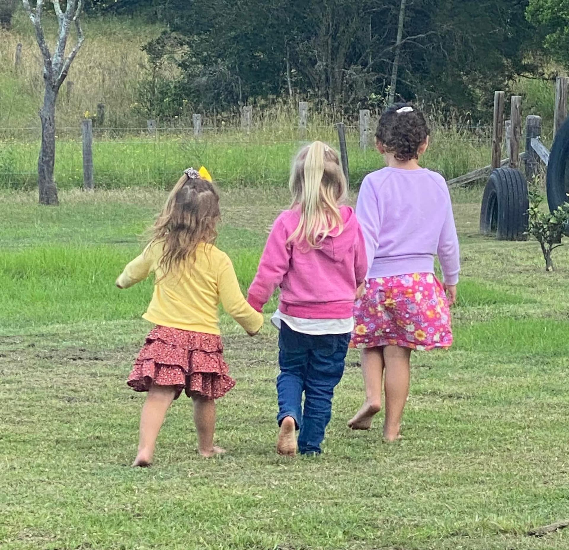 Three young girls walking hand-in-hand across a grassy field — Earth Angels Child Care Centre in Tinonee, NSW