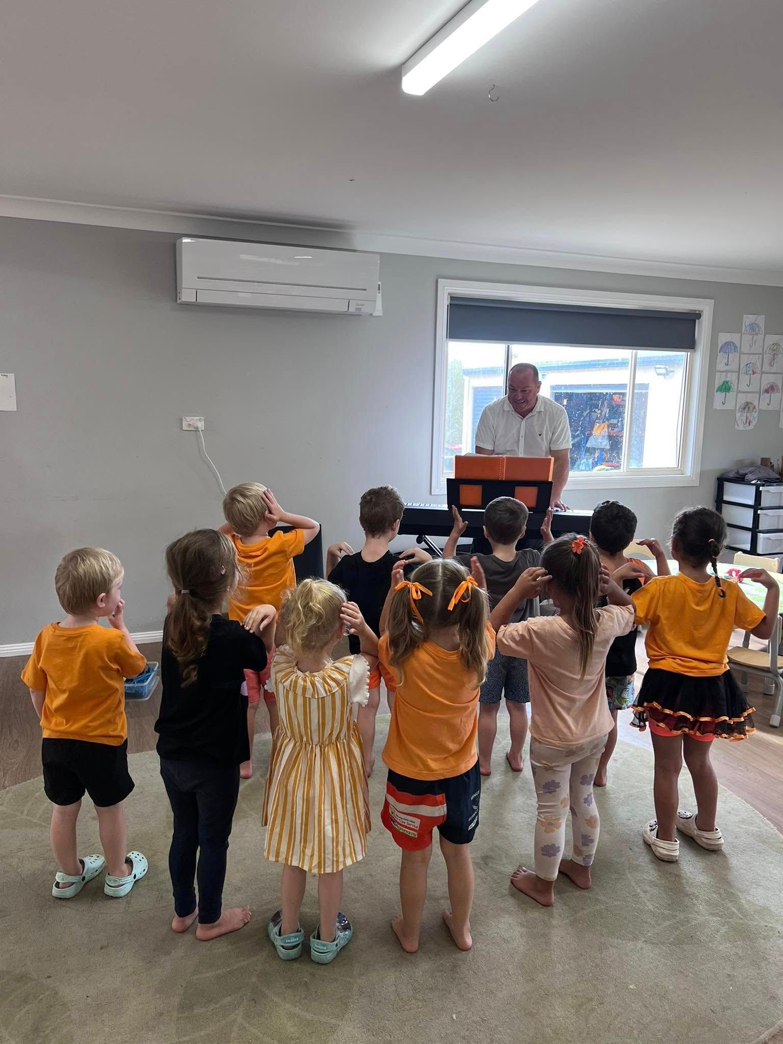 A Group of Children Are Standing in a Circle in Front of a Man Playing an Organ — Earth Angels Child Care Centre in Tinonee, NSW