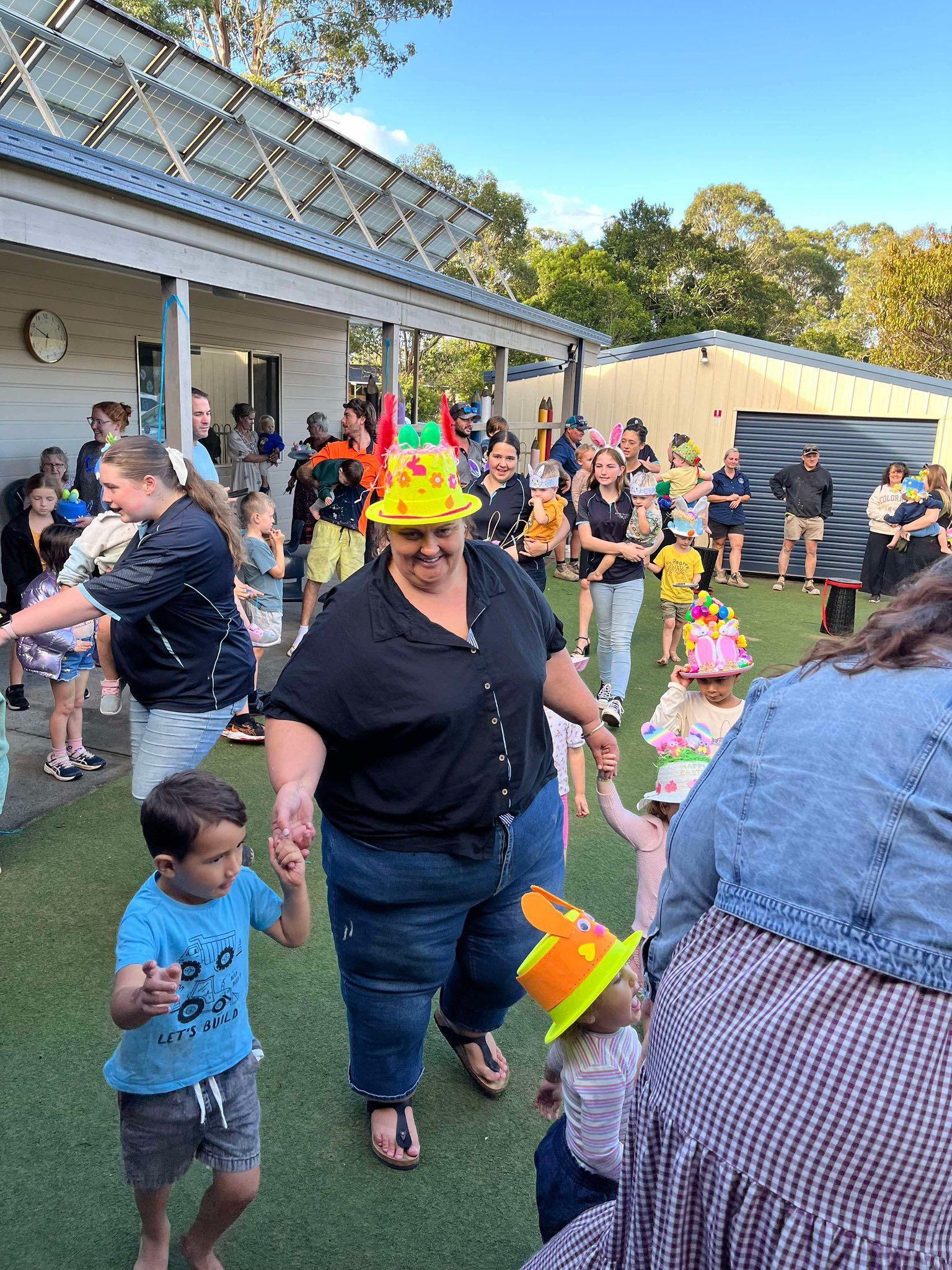 A Woman Wearing a Clown Hat is Walking With a Group of Children — Earth Angels Child Care Centre in Tinonee, NSW