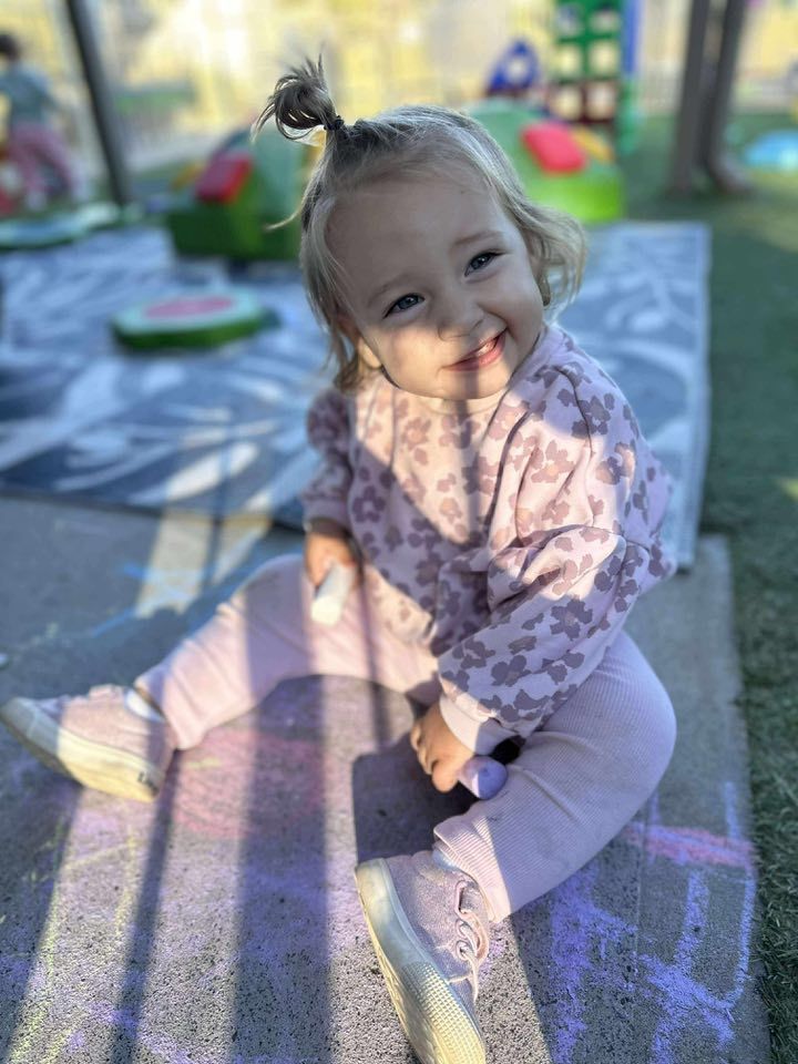 A Little Girl is Sitting on the Ground Playing With Chalk — Earth Angels Child Care Centre in Tinonee, NSW